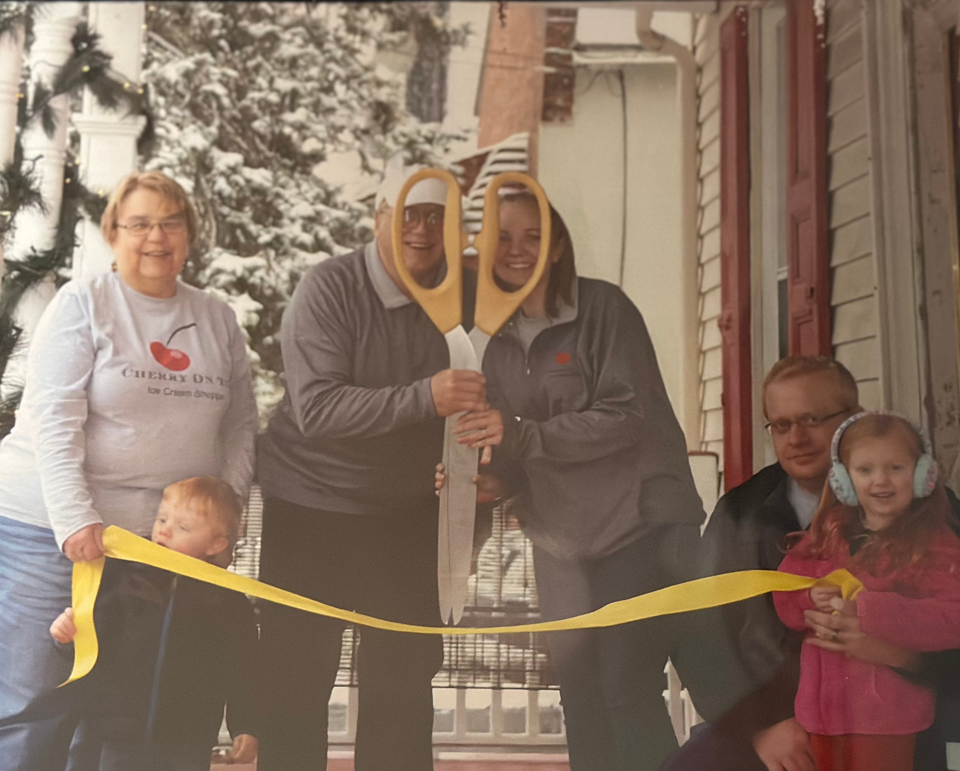 The family cutting the ribbon with giant scissors at the snowy December 2017 grand opening